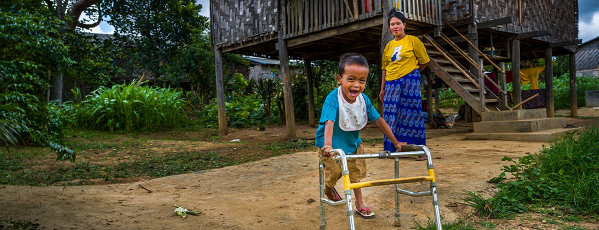 Image of young boy using a walker and an adult watching in the background
